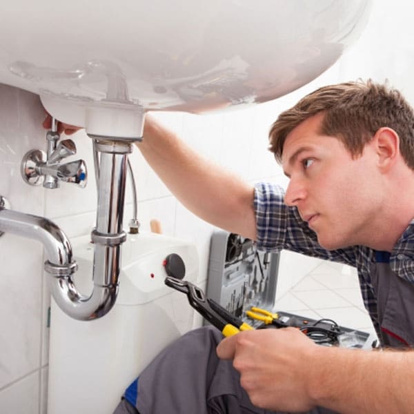 stock photo of person holding wrench and looking at pipes under bathroom sink