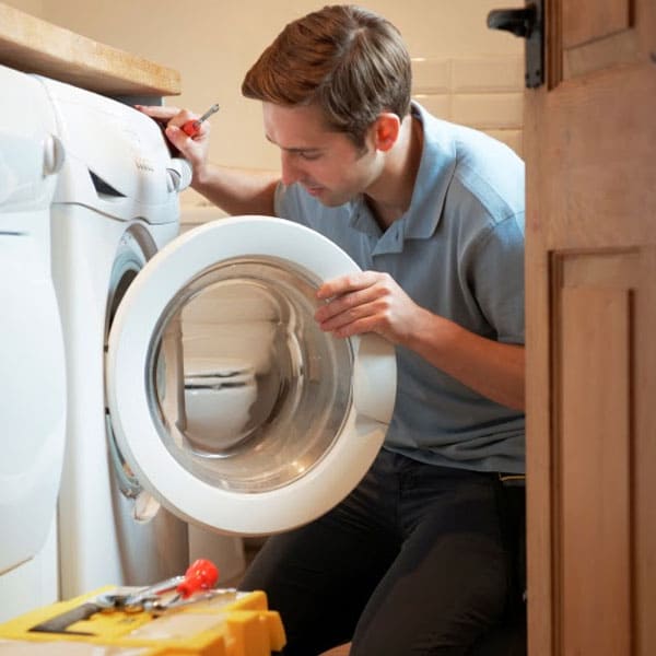stock photo of person looking into front loading washing machine with screwdriver in hand and tool box on floor